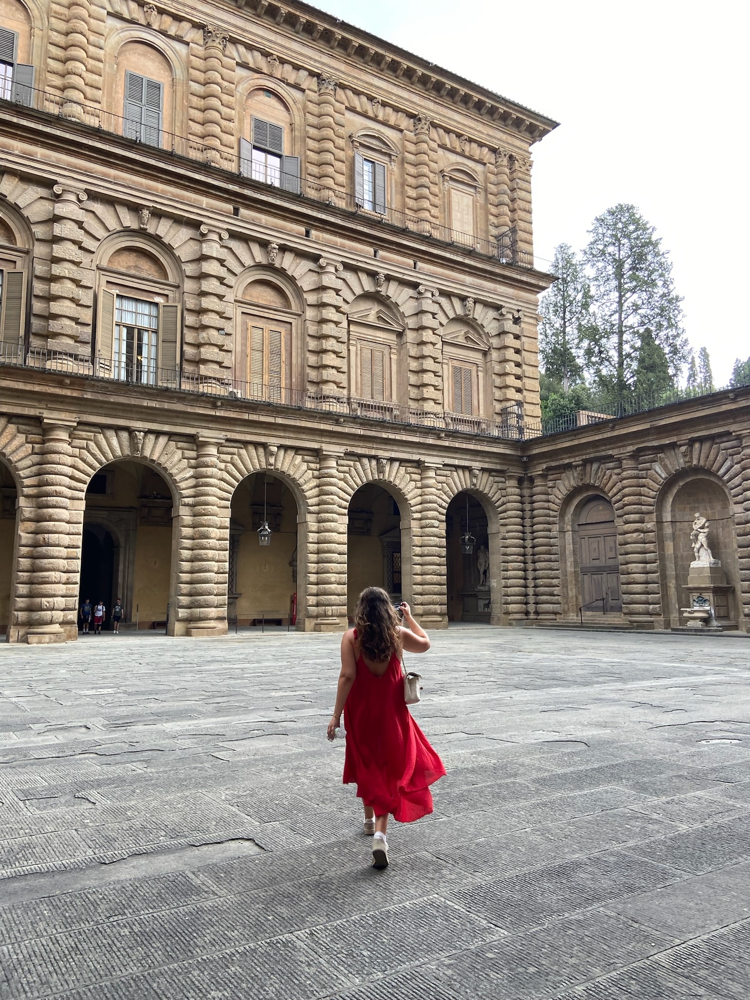 Picture of a woman in a flowy red dress walking through a medieval palace in Florence